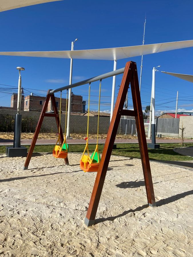 Columpios de madera con asientos de colores, instalados en área de arena