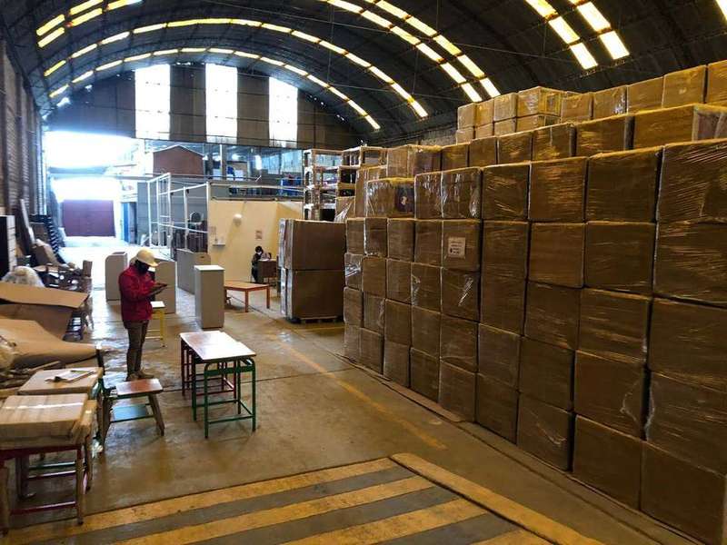 Almacén con pared de cajas embaladas y personal supervisando la producción