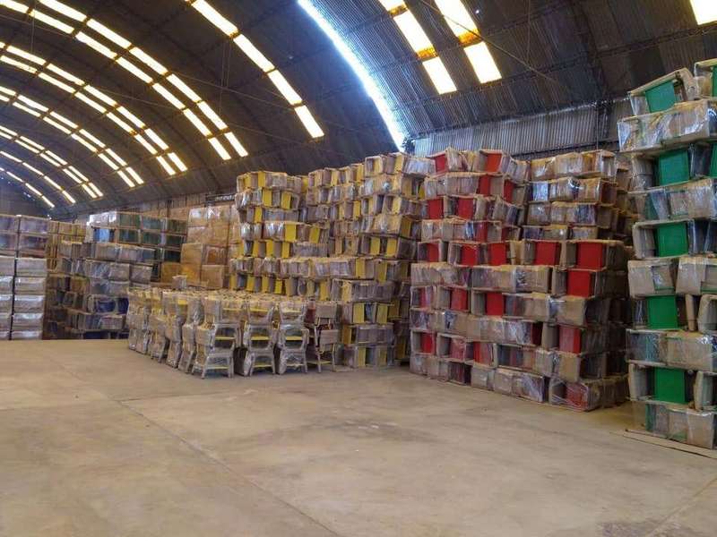 Almacén con sillas escolares de colores embaladas, apiladas en altura